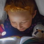 Child reading beneath a blanket with a flashlight, representing prepper books for young kids