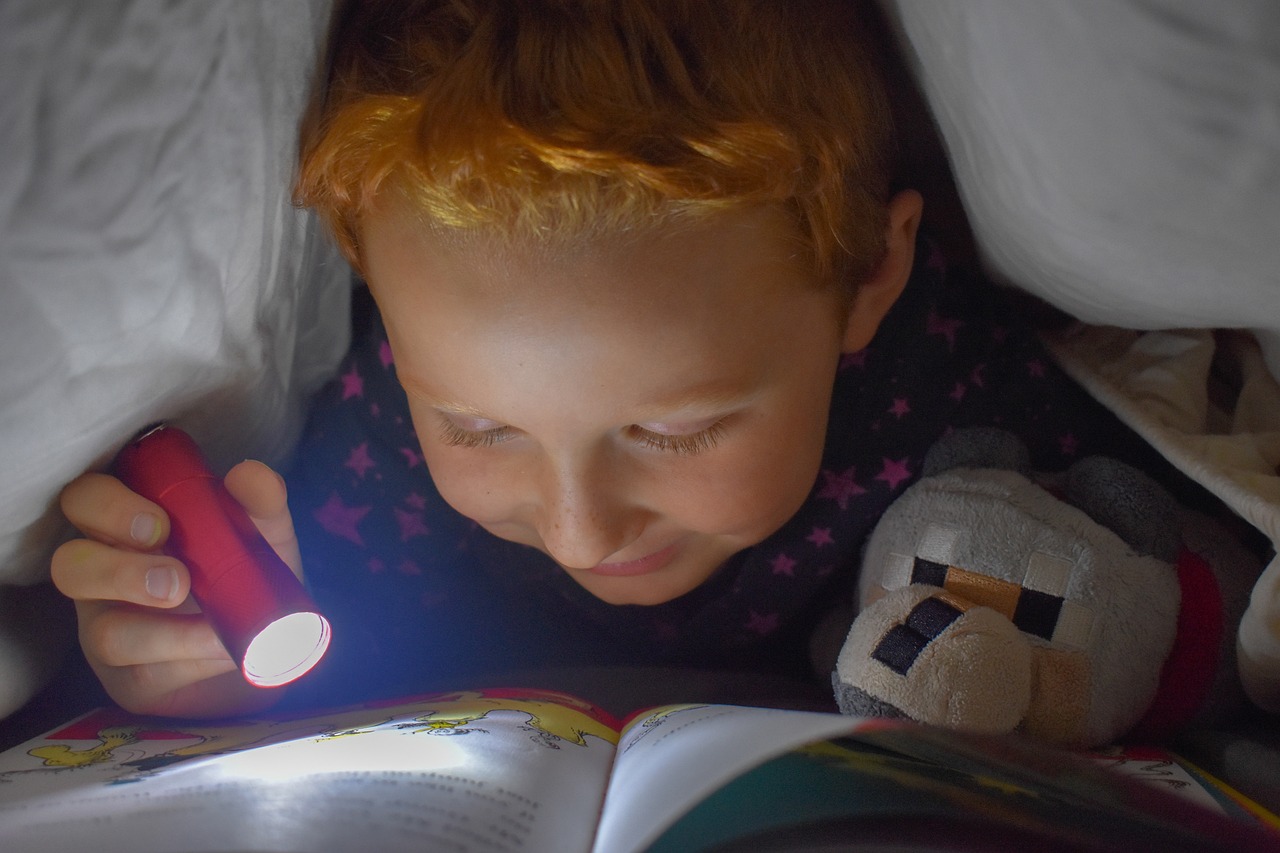 Child reading beneath a blanket with a flashlight, representing prepper books for young kids