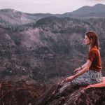 A woman meditating on top of a mountain, representing How to Manage Stress