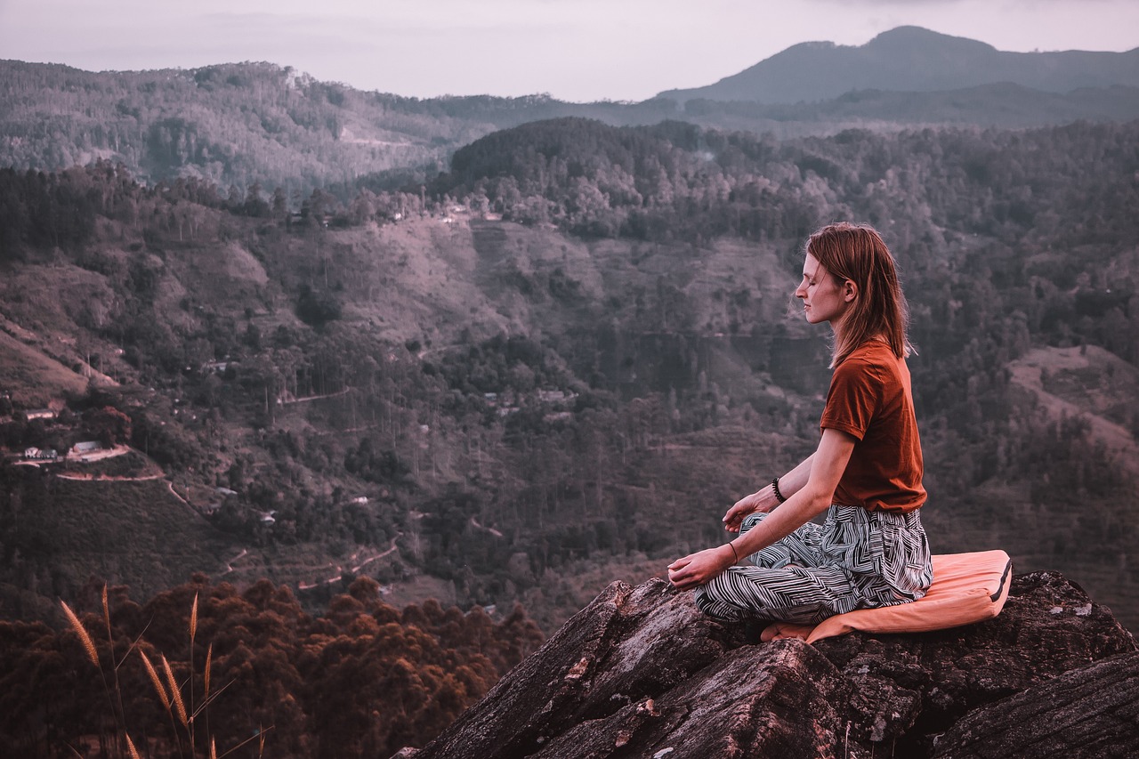 A woman meditating on top of a mountain, representing How to Manage Stress